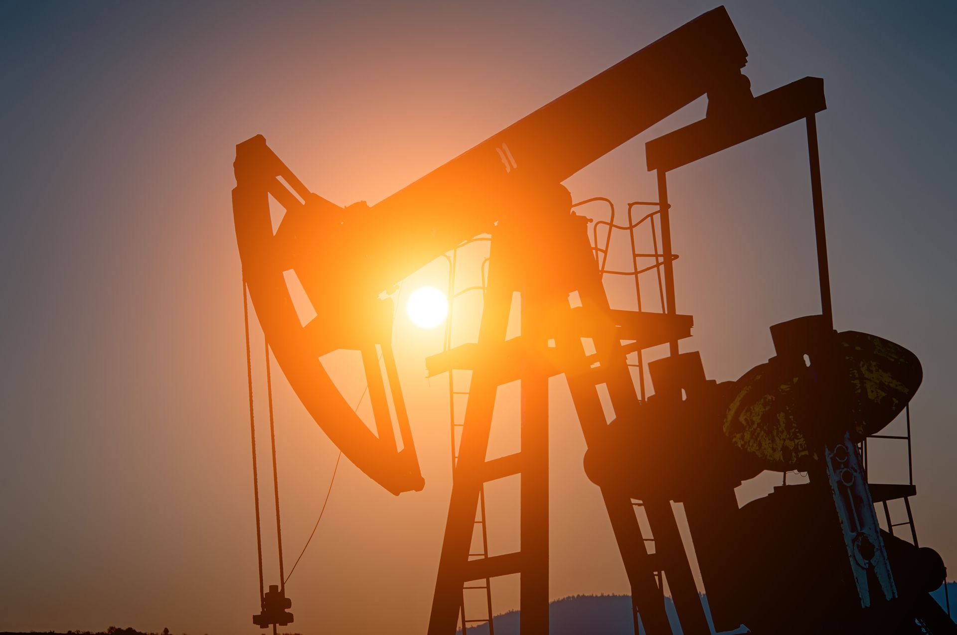 A silhouette of an oil pump at sunset with the sun shining through it.