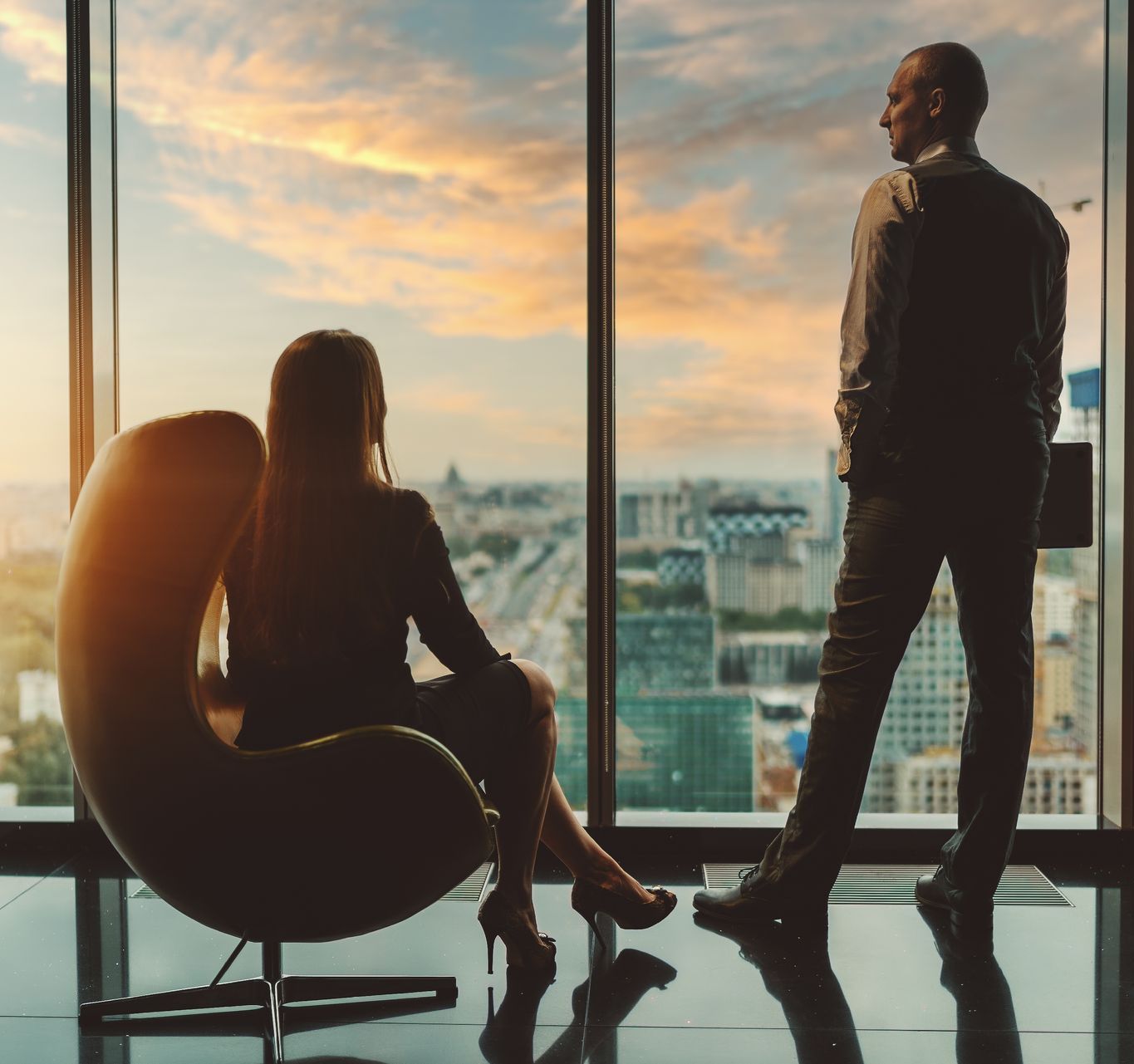 A man and a woman are looking out of a window at sunset.