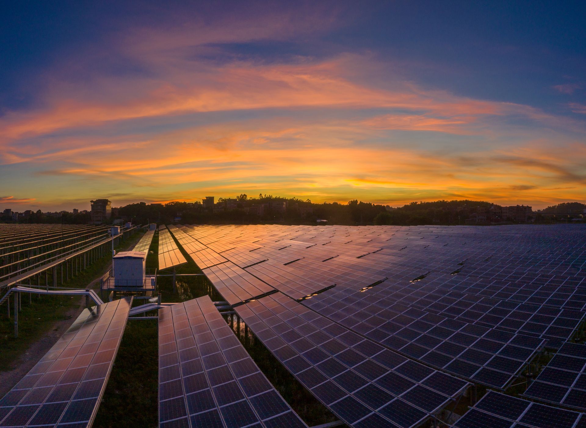 A field of solar panels with a sunset in the background.