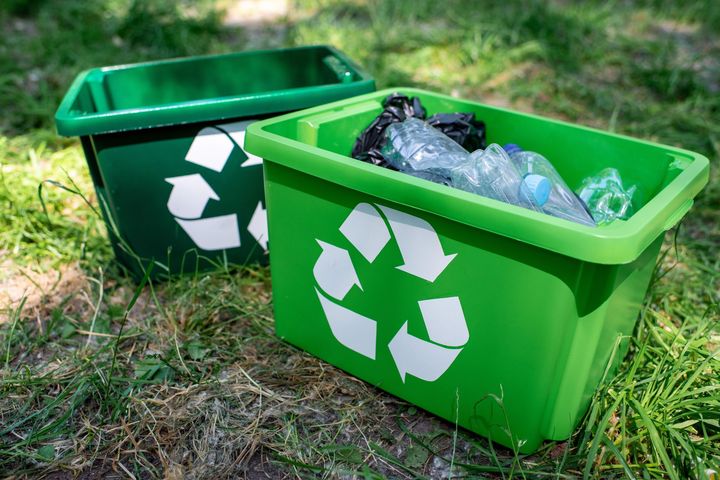 Dos contenedores de reciclaje verdes llenos de botellas de plástico están tirados en el césped.