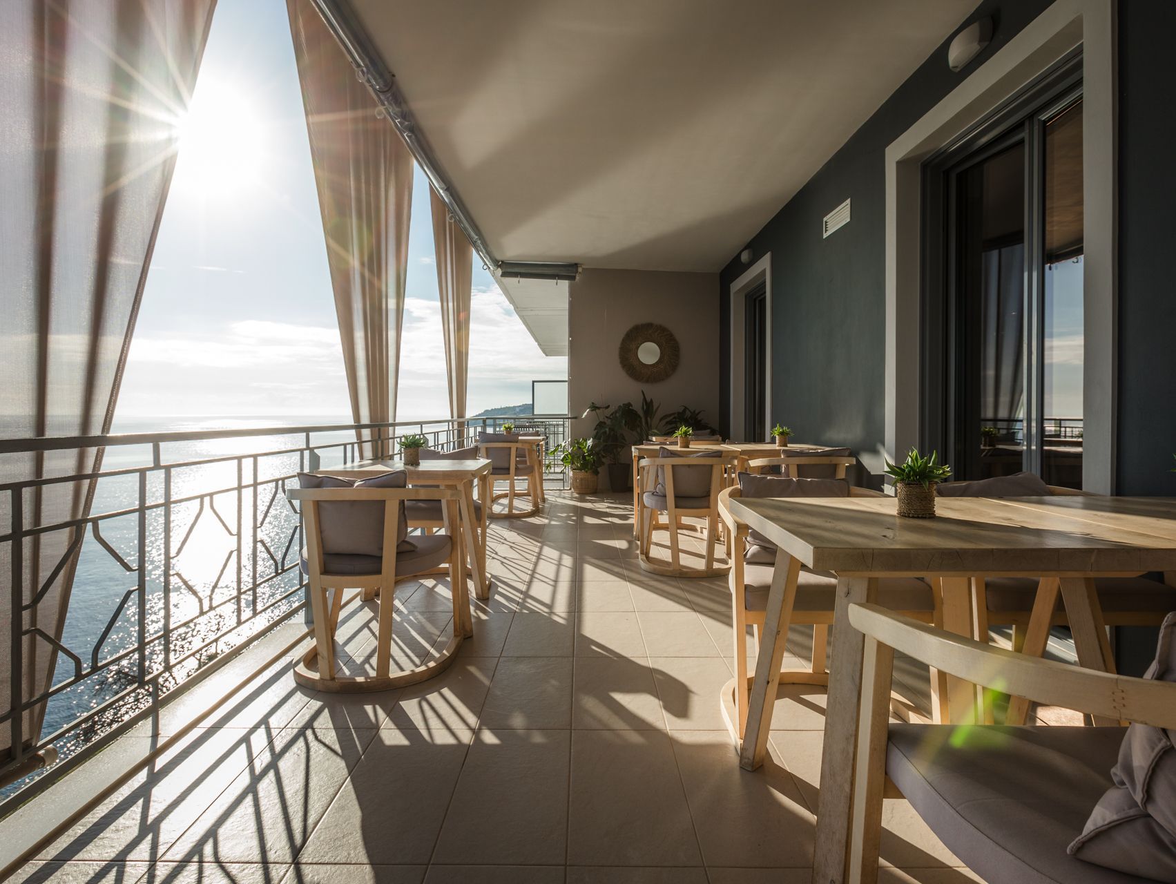 A large balcony with tables and chairs overlooking the ocean.