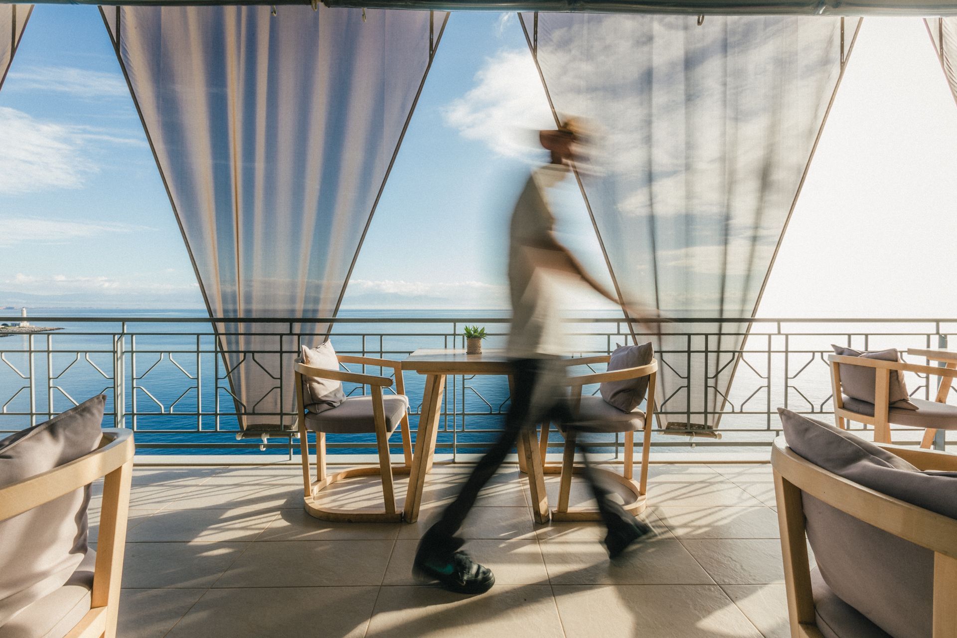 A blurry picture of a man walking on a balcony overlooking the ocean.
