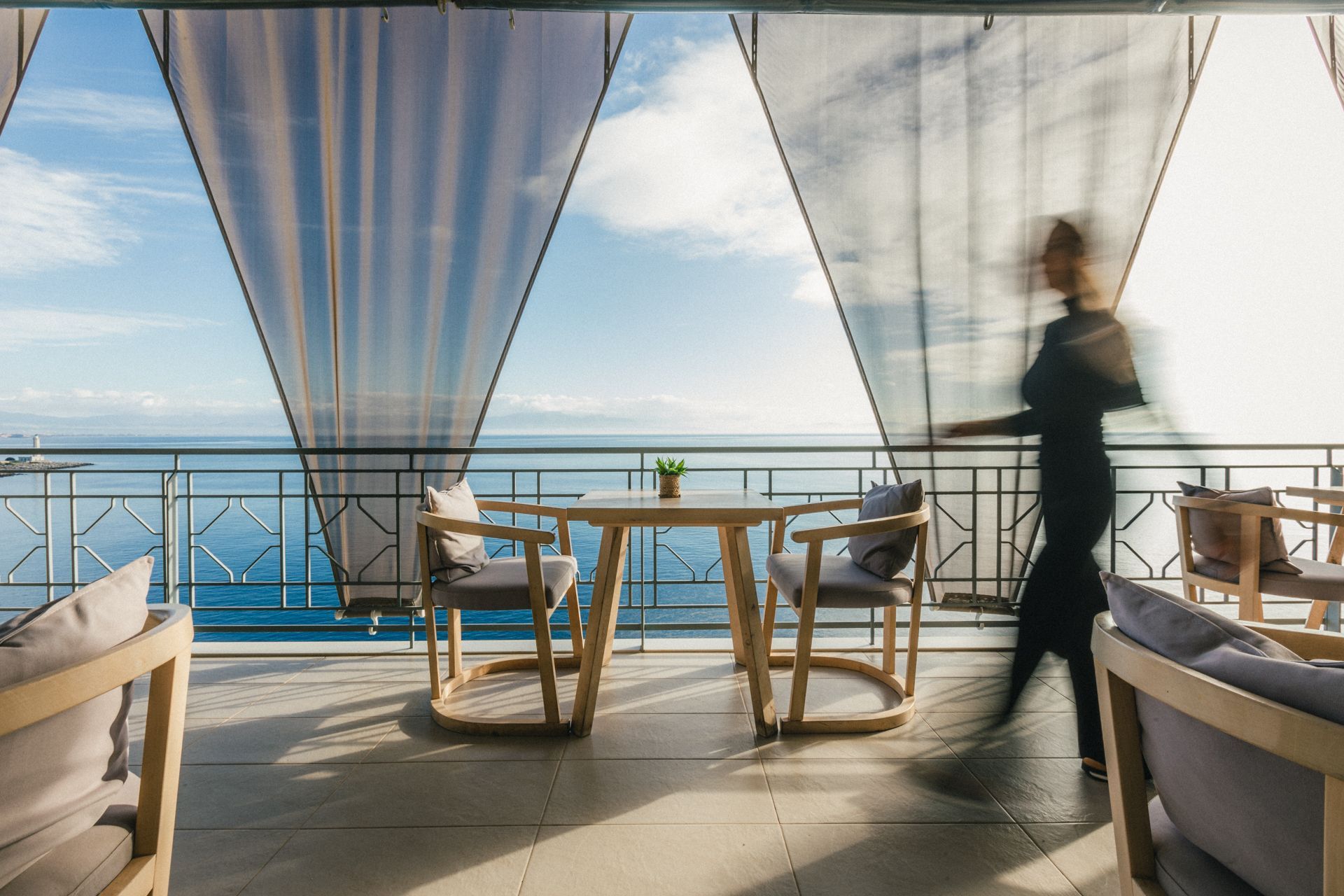A waitress is serving food on a balcony overlooking the ocean.