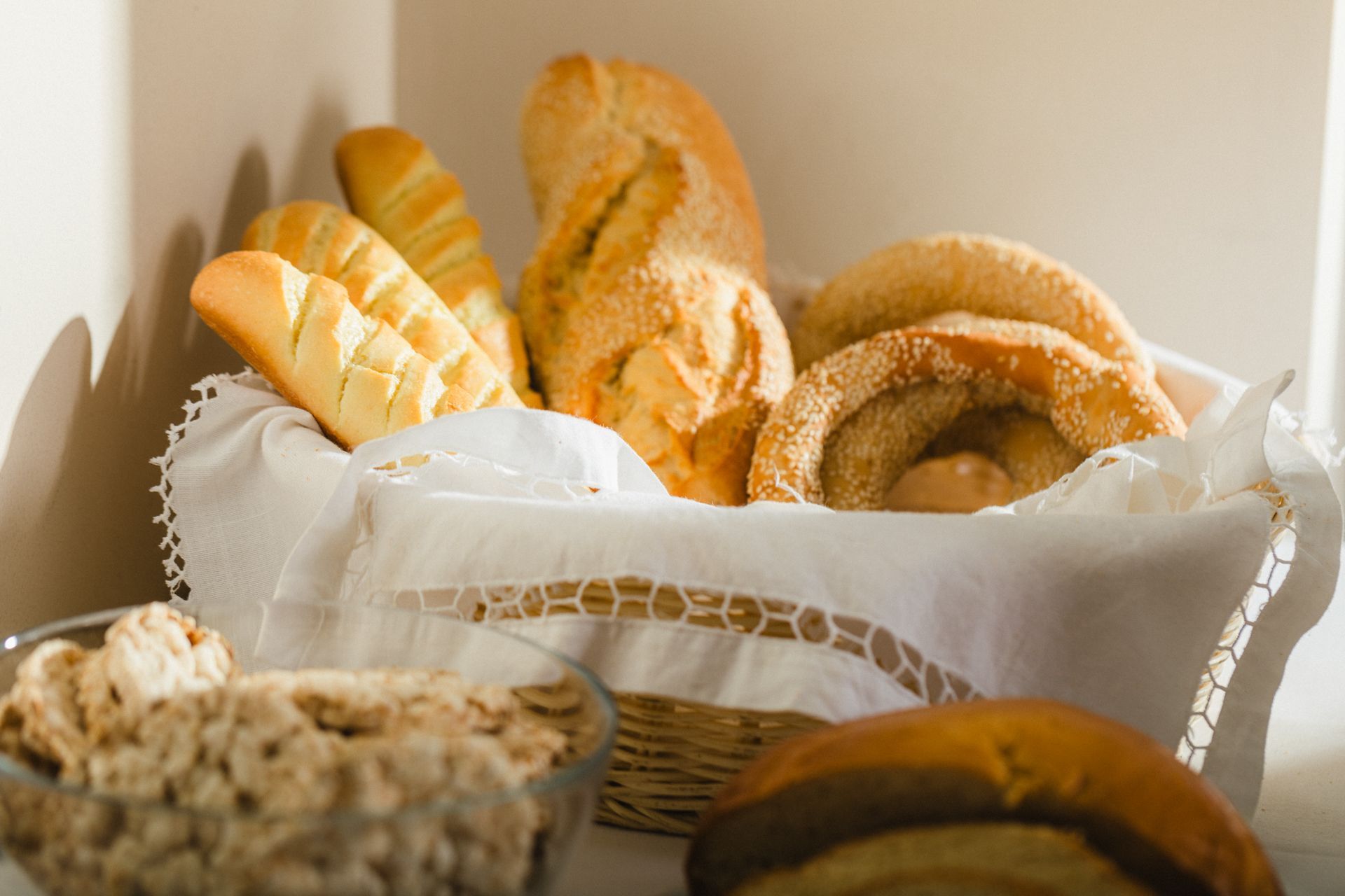 A basket of bread is sitting on a table next to a bowl of cereal.