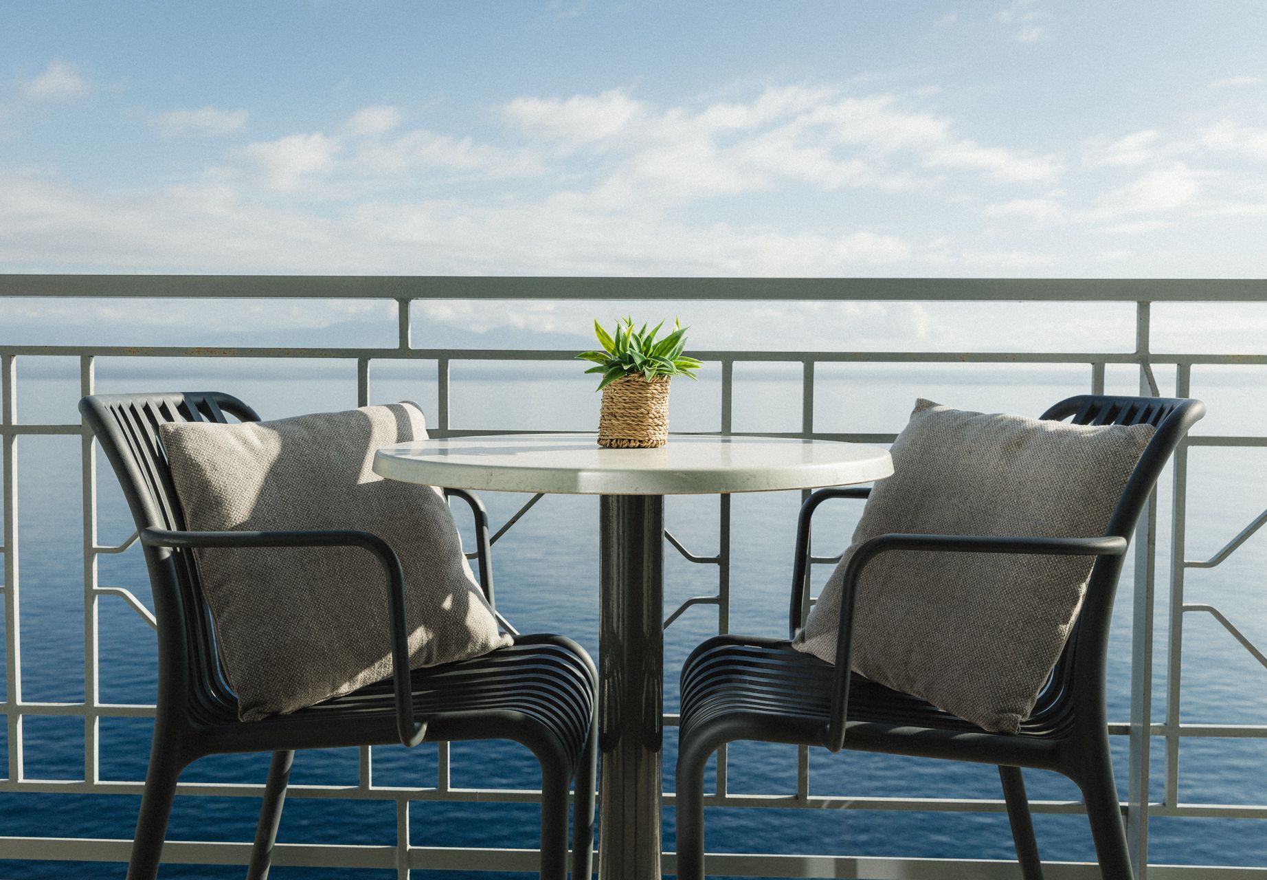 Two chairs and a table on a balcony overlooking the ocean.