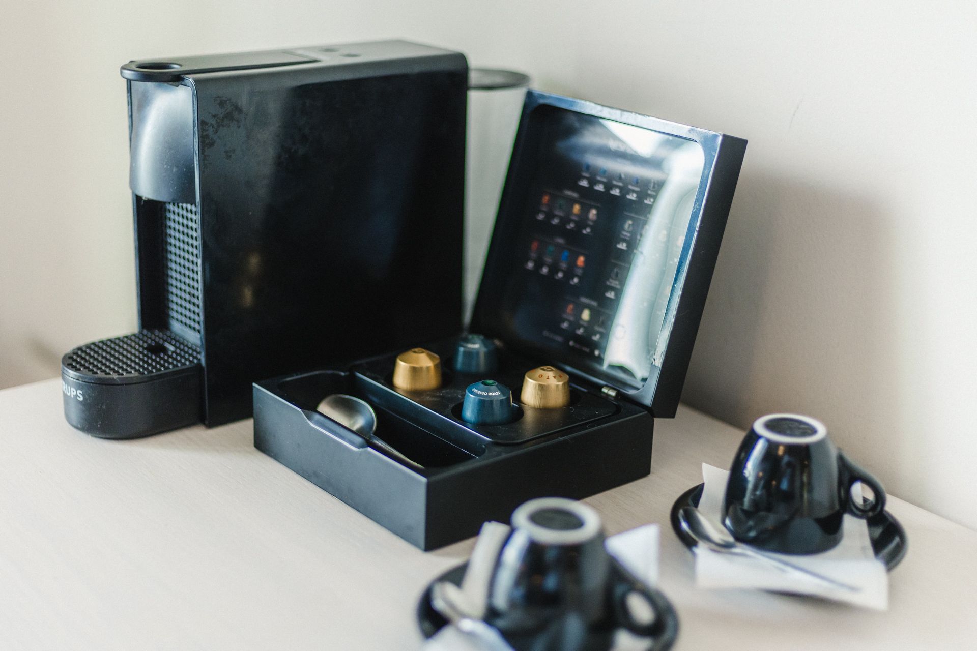 A coffee maker is sitting on a table next to two cups and saucers.