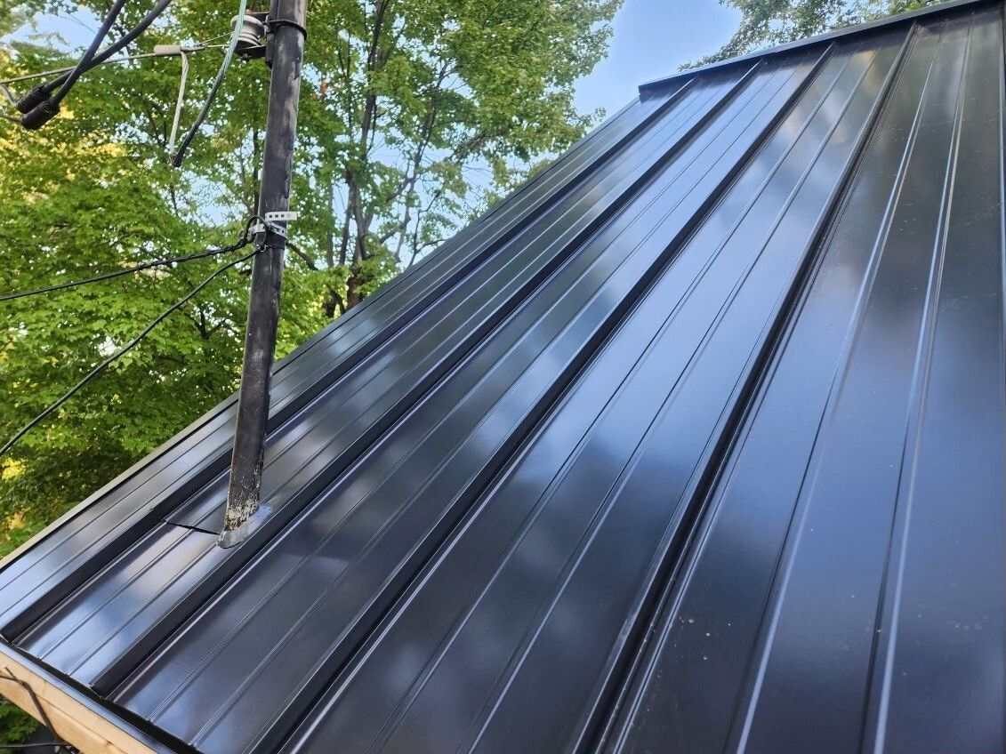 Toit en métal noir à nervures verticales ; lignes électriques en arrière-plan.