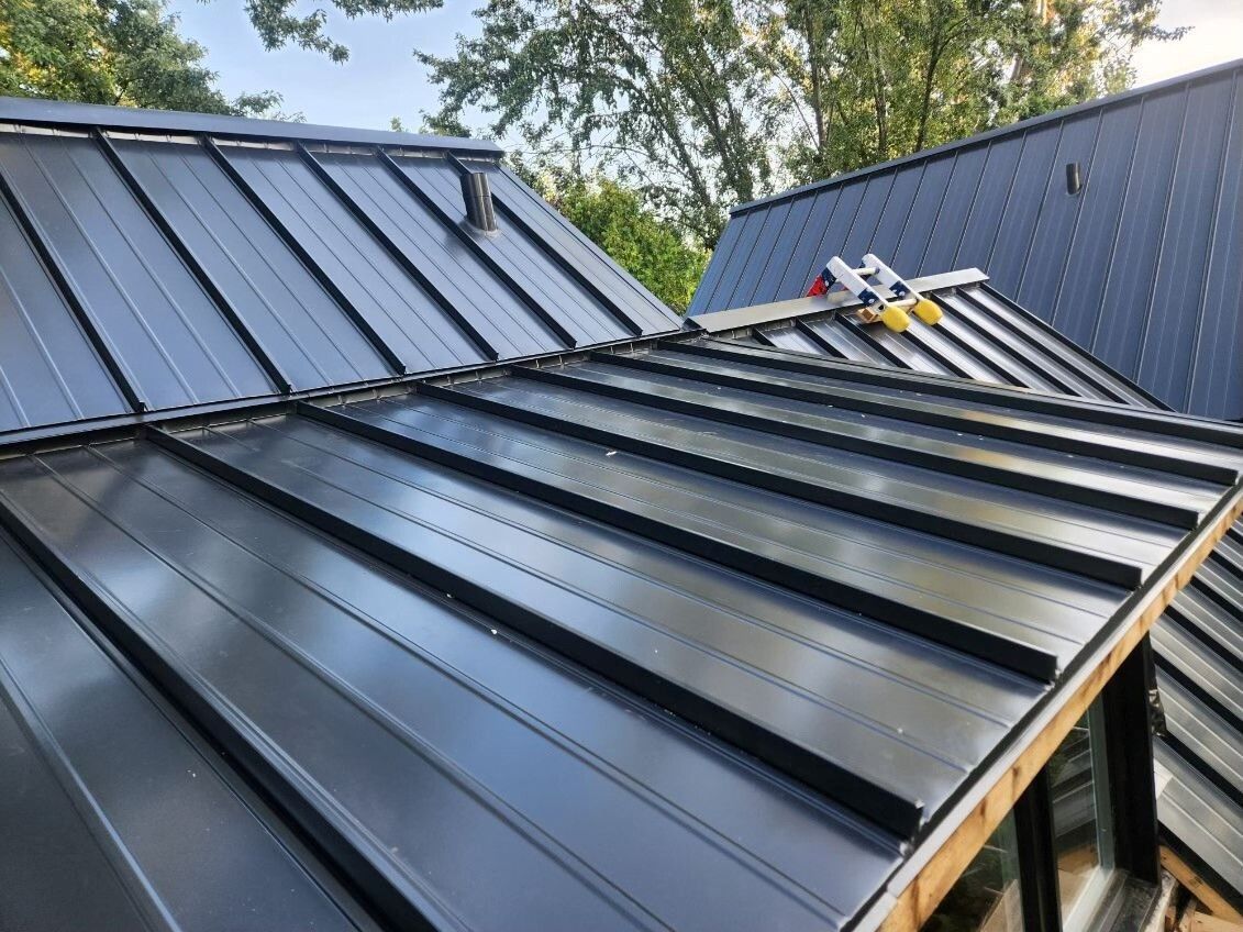 Toiture métallique noire d'une maison, vue en angle. Des outils sont posés sur le toit. Cadre extérieur ensoleillé.