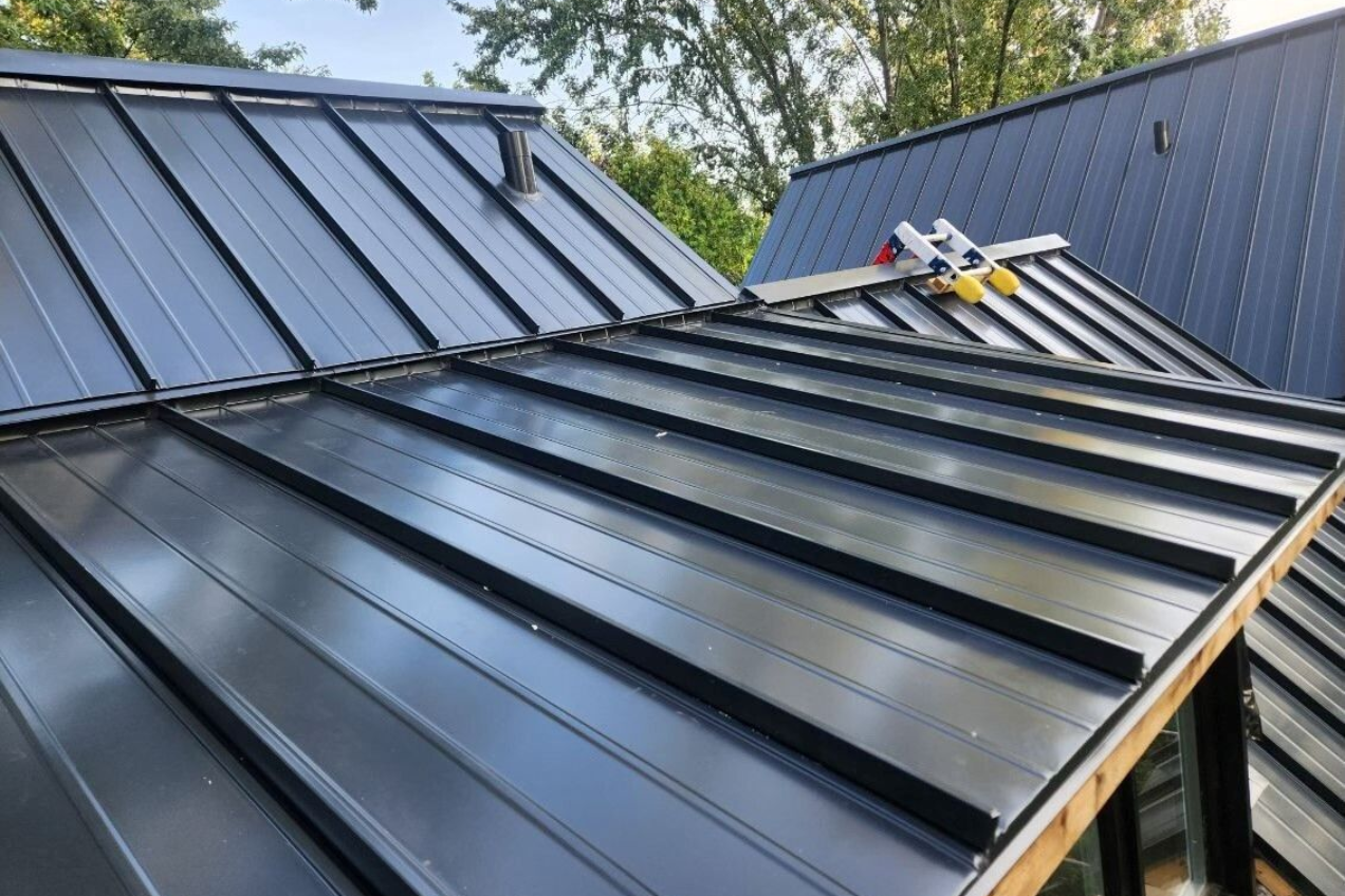 Toiture métallique gris foncé sur un bâtiment se détachant sur un fond vert vif.