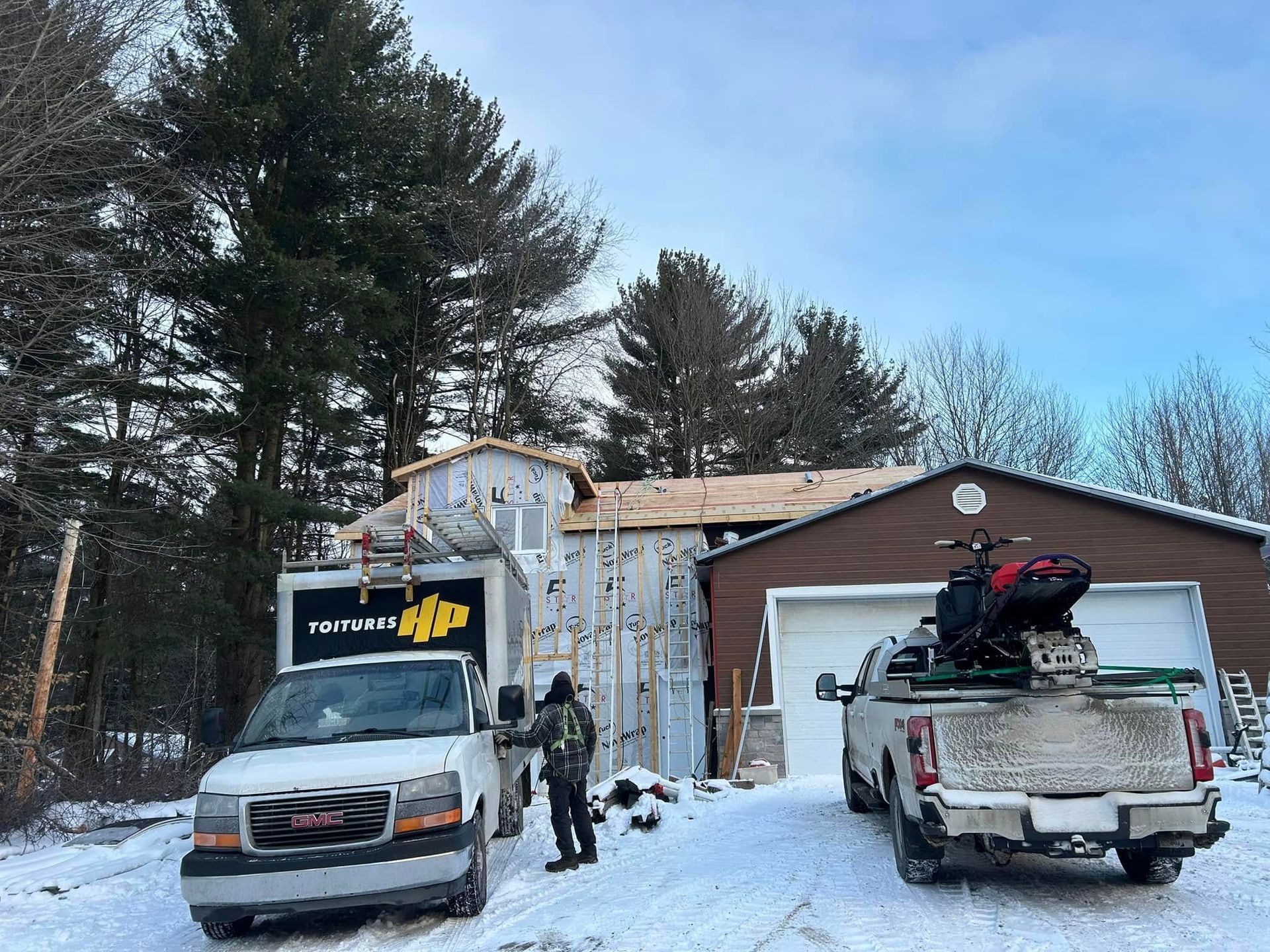 Deux camions sont garés devant une maison sous la neige.