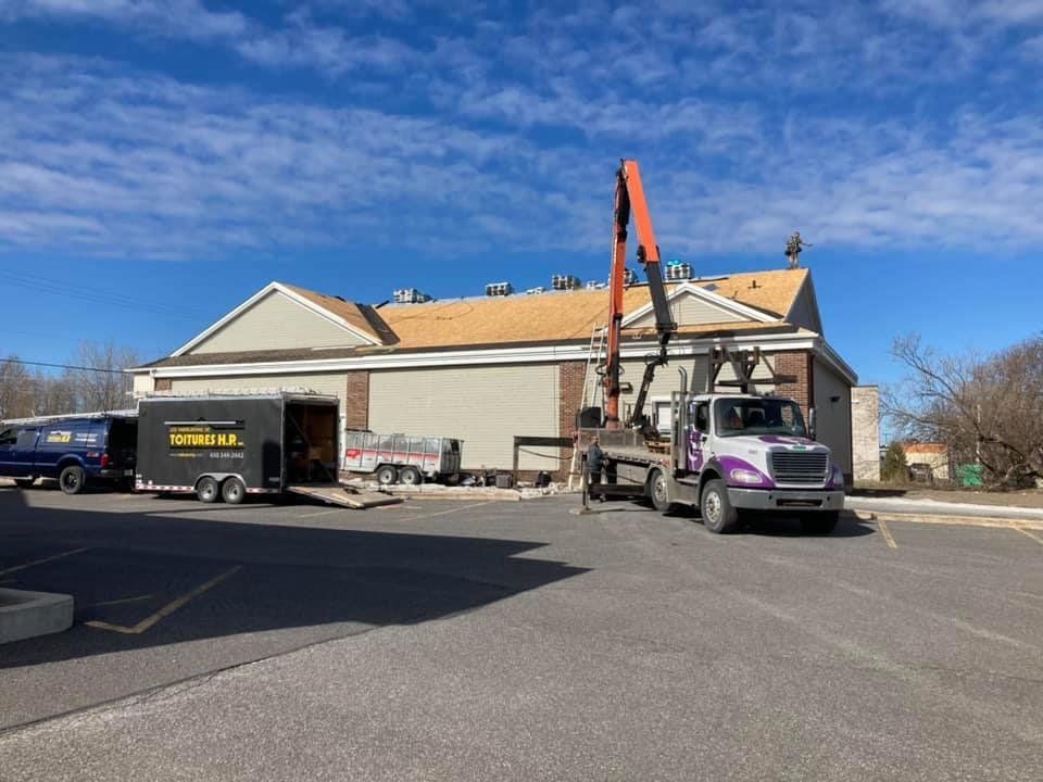 Un camion avec une grue à l'arrière est garé devant un bâtiment.