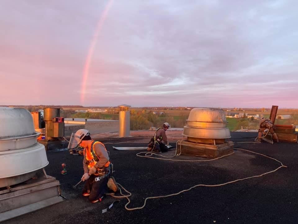 Deux hommes travaillent sur un toit avec un arc-en-ciel dans le ciel.