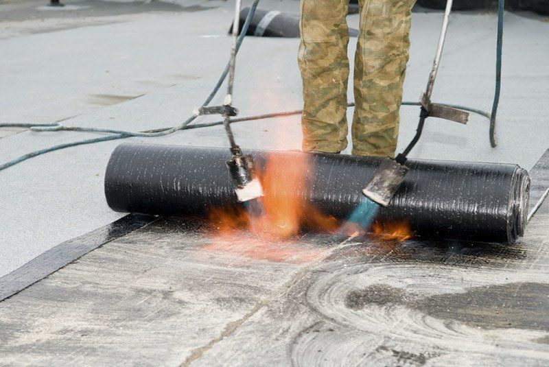 Une personne enroule un rouleau de matériau de toiture sur un toit avec une torche.