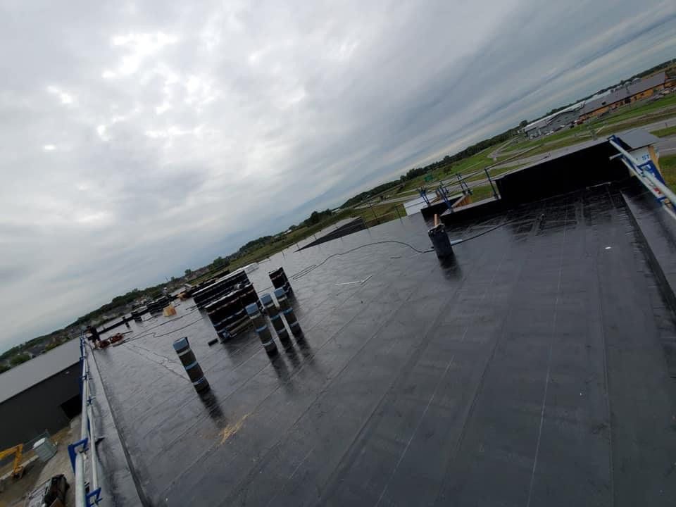 Un toit noir avec beaucoup de tuyaux dessus et un ciel nuageux en arrière-plan.