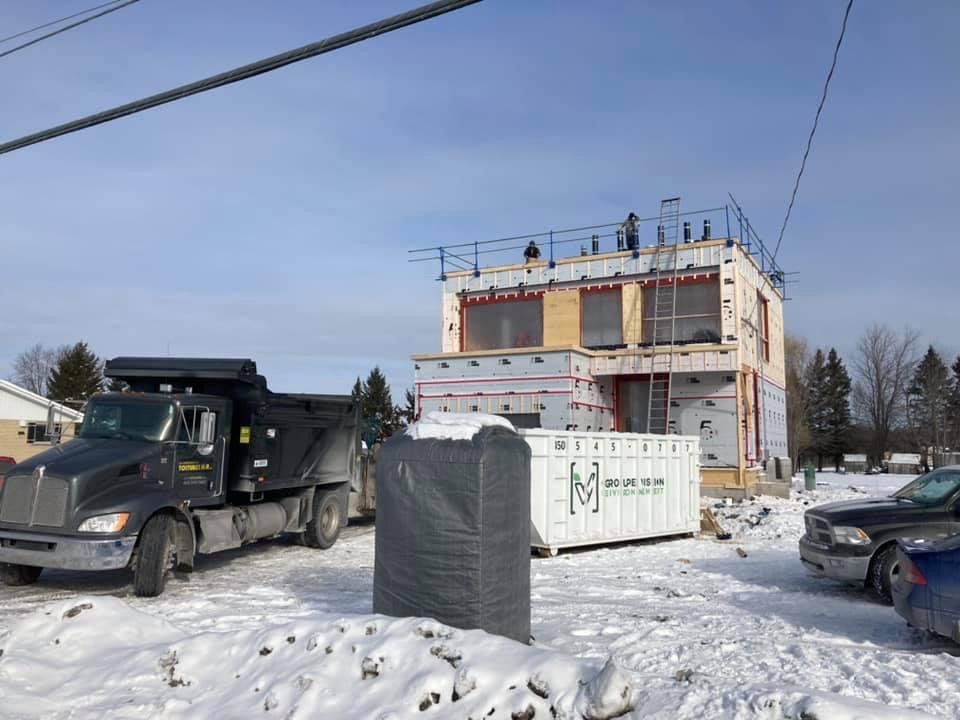 Un camion benne est garé devant une maison en construction sous la neige.