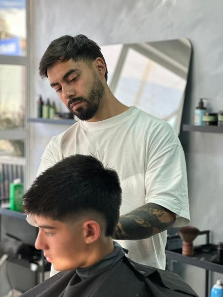 Un barbero concentrado, vestido con una camiseta blanca, peina a un cliente en una barbería moderna y bien iluminada.