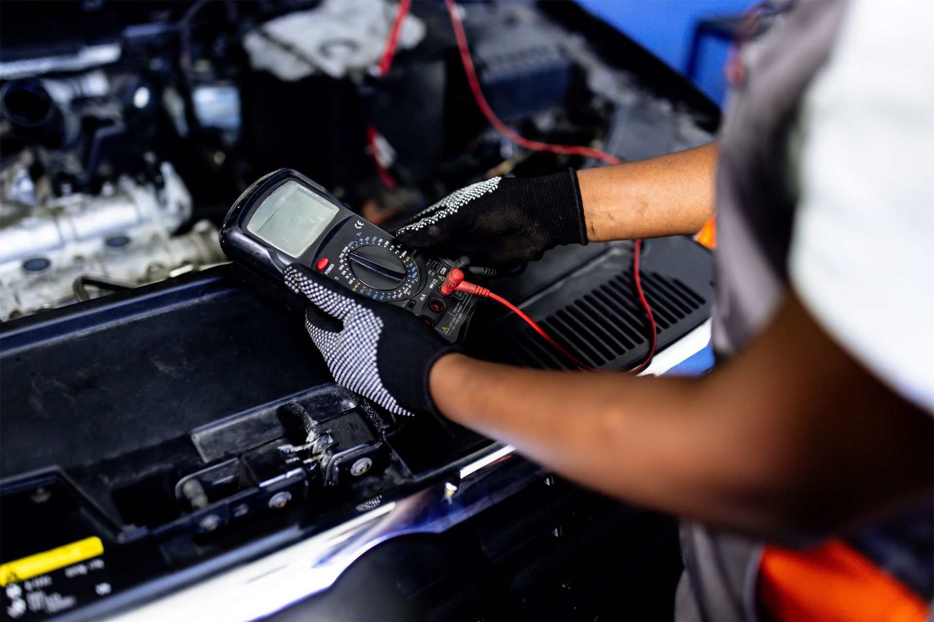 A mechanic is working on a car with a multimeter.