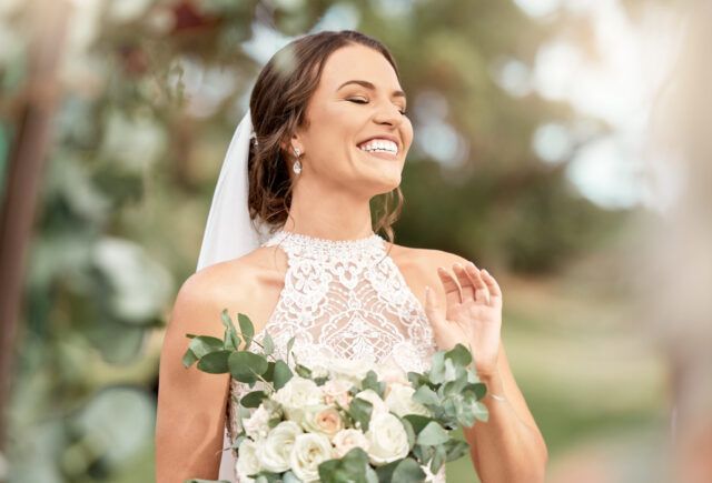 A bride in a wedding dress is holding a bouquet of flowers and smiling.