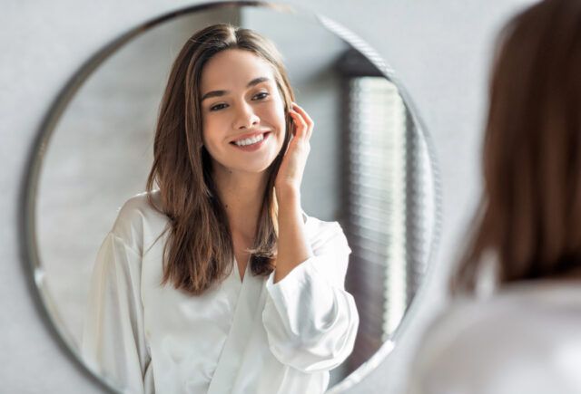 A woman is smiling while looking at herself in a mirror.