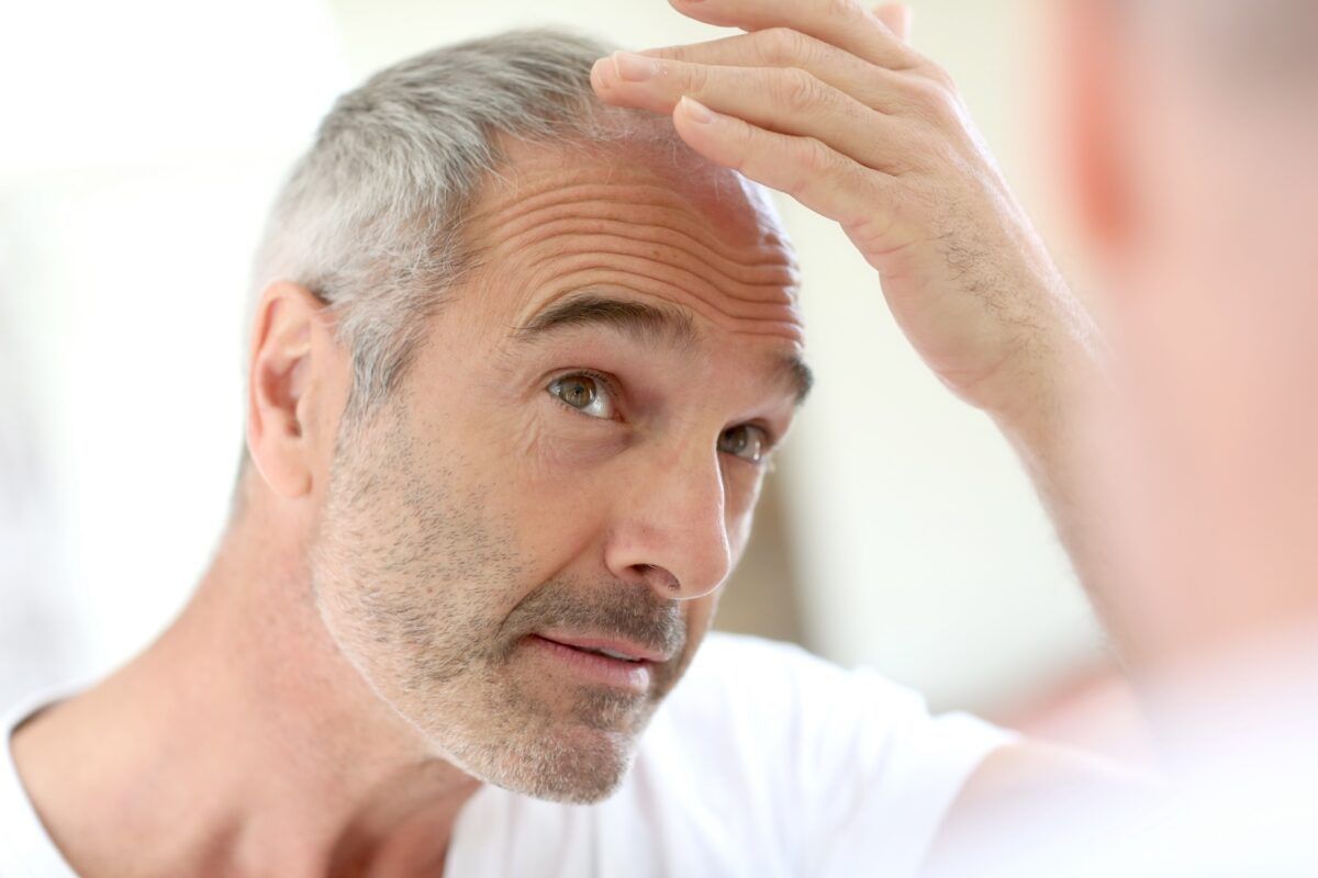 A man is looking at his hair in the mirror.