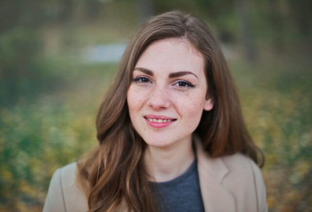 A woman in a tan coat is smiling for the camera.