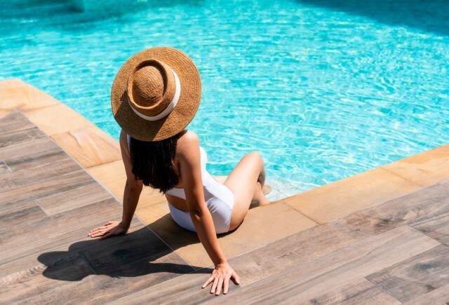 A woman in a straw hat is sitting on the edge of a swimming pool.