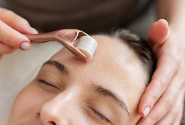 A woman is getting a facial treatment with a roller on her forehead.