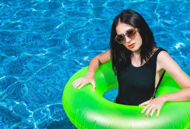 A woman in a black swimsuit is floating on an inflatable ring in a swimming pool.