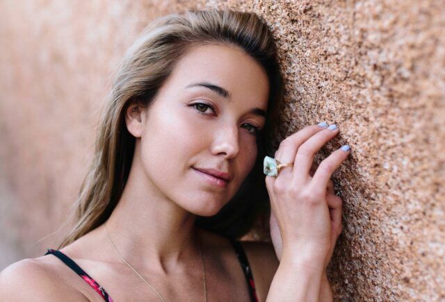 A woman wearing a ring is leaning against a wall.