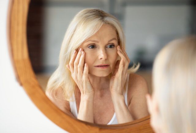 A woman is looking at her face in a mirror.