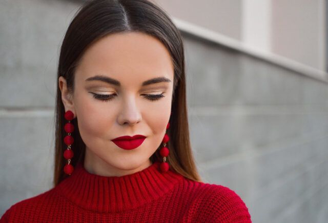 A woman wearing a red sweater and red earrings is looking down.