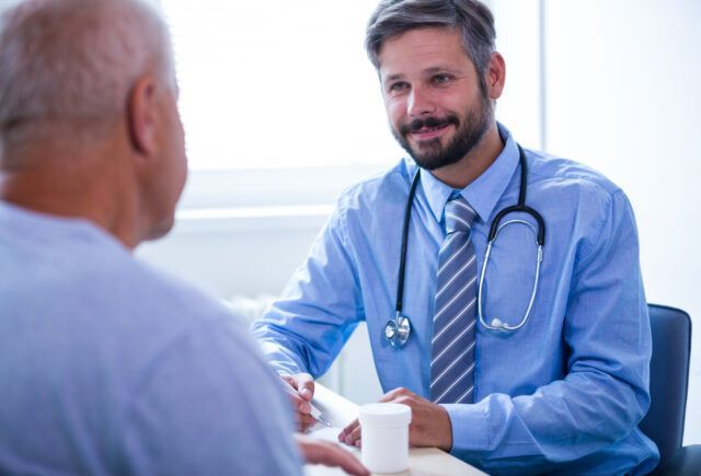 A doctor is sitting at a table talking to a patient.