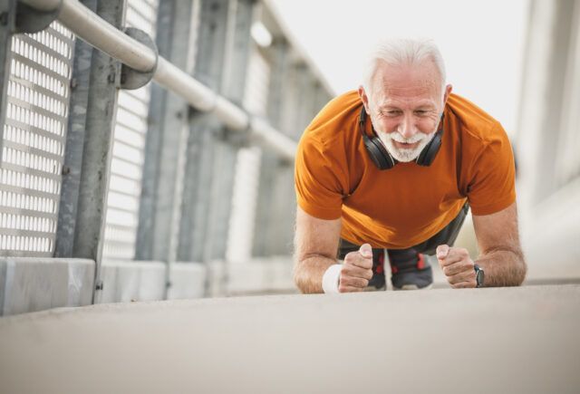 An older man is doing push ups on a sidewalk.