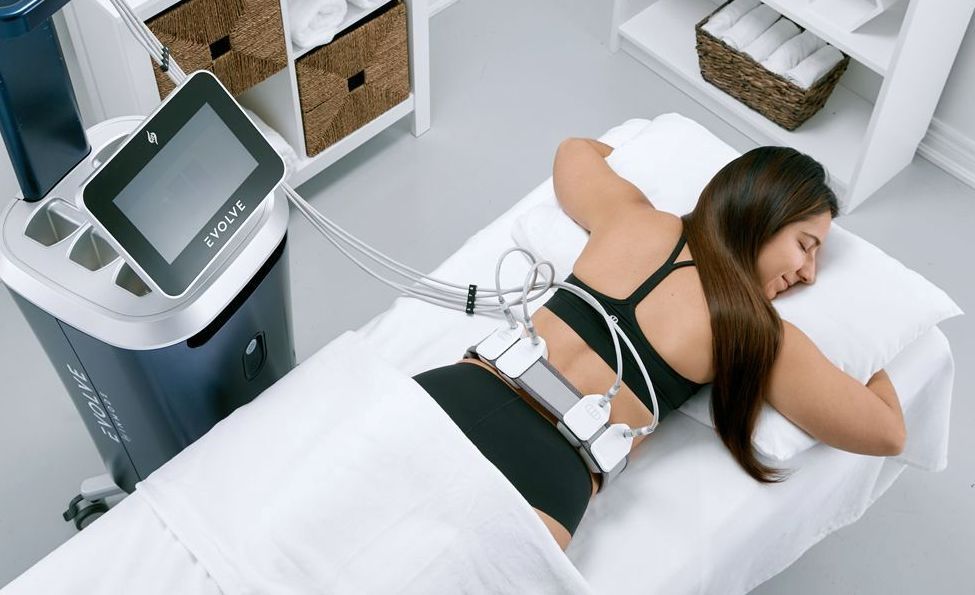 A woman is laying on a bed with a machine on her back.