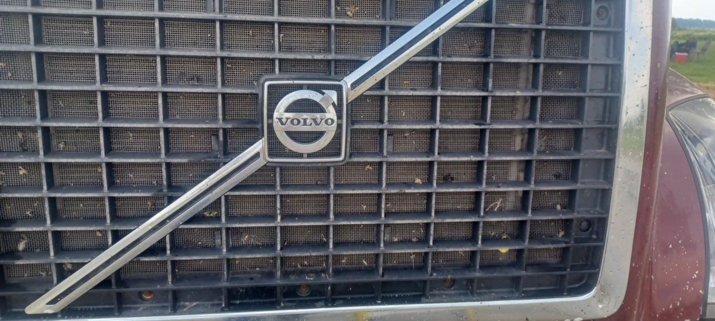 Close-up of a Volvo truck grill with the Volvo logo centered. The grill is metallic gray with a diagonal silver bar.