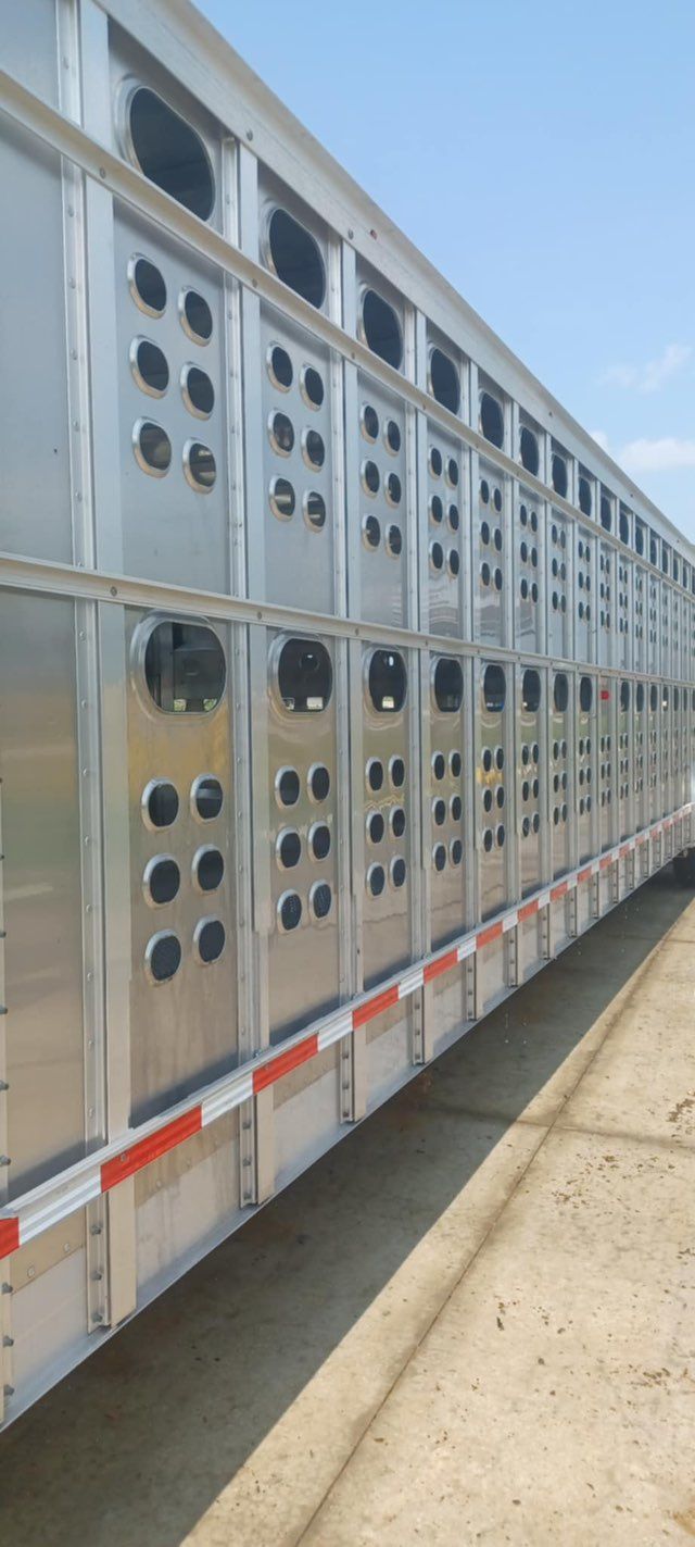 Side view of a silver livestock trailer with multiple openings. It's parked outside on a bright day.