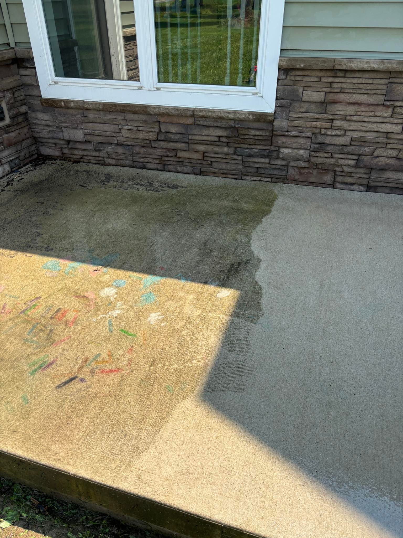 Concrete patio with wet and dry areas, next to a building with stone and a window.