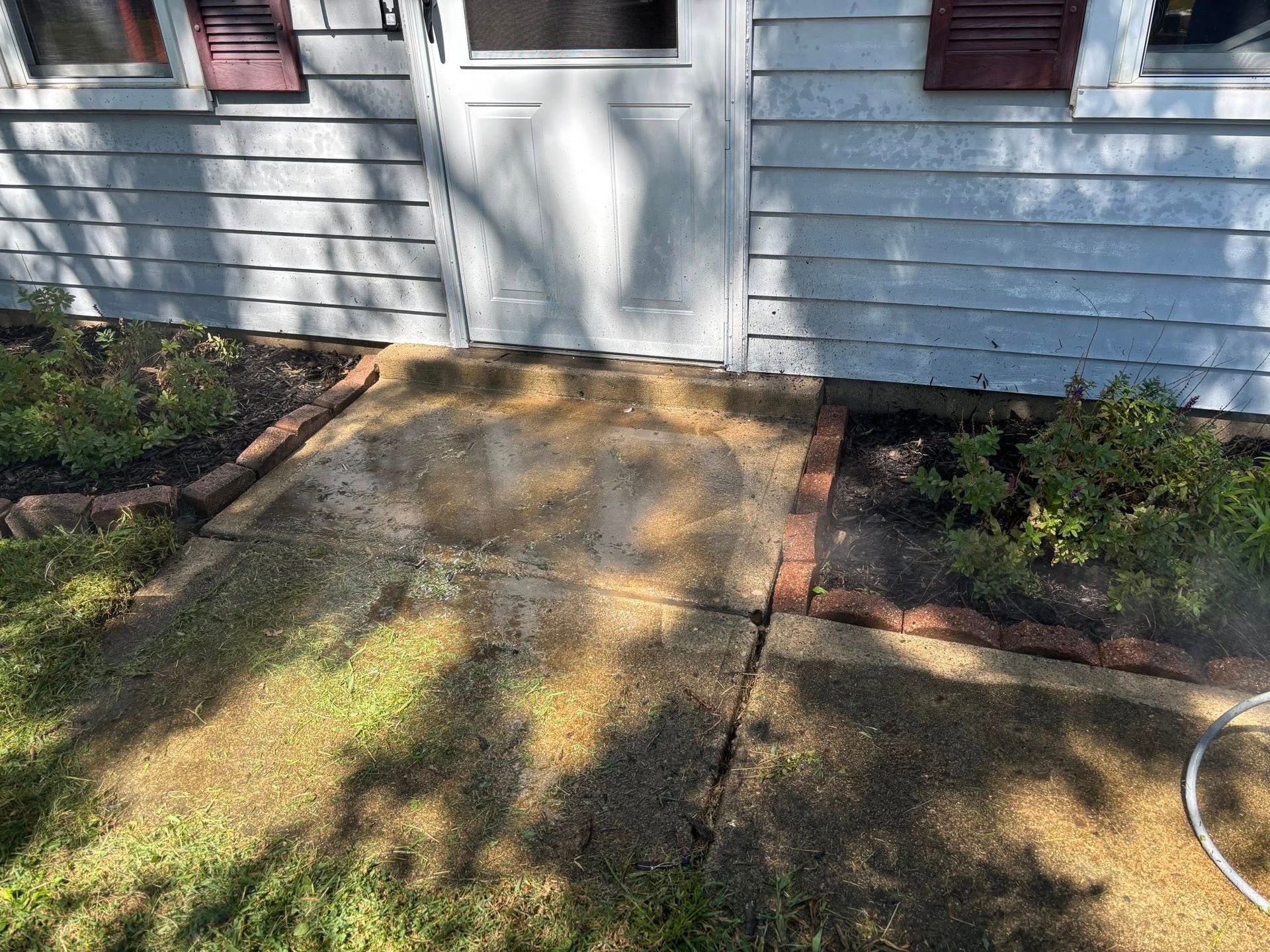 Concrete walkway leading to a house door with landscaping, including grass, plants, and brick edging.