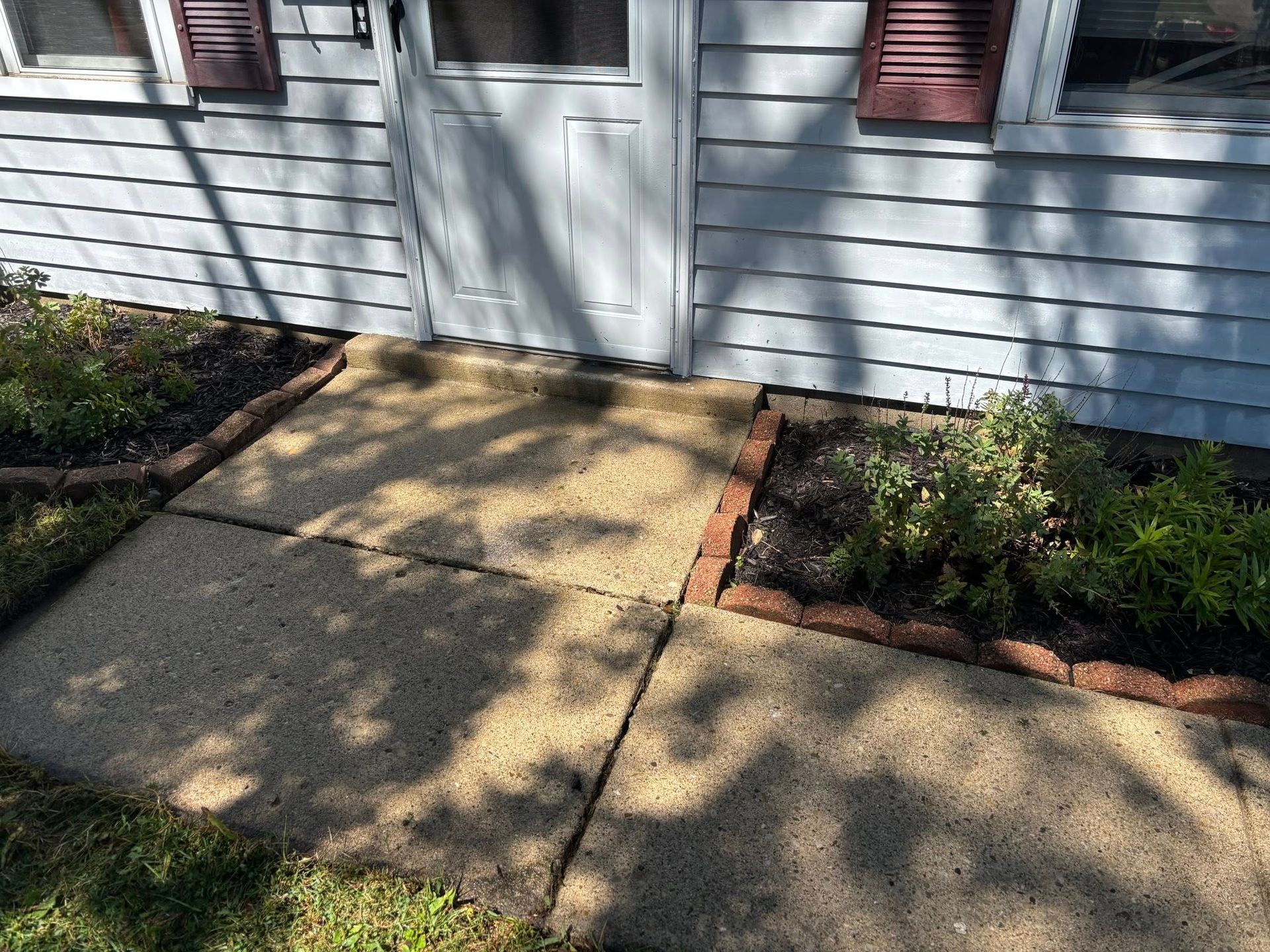 A concrete walkway in front of a white door with two small garden beds on either side.