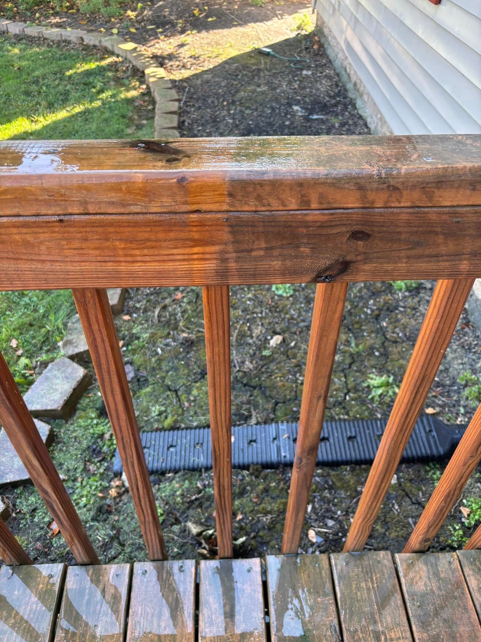 Wooden deck railing, partially cleaned, showing weathered wood and surrounding yard.
