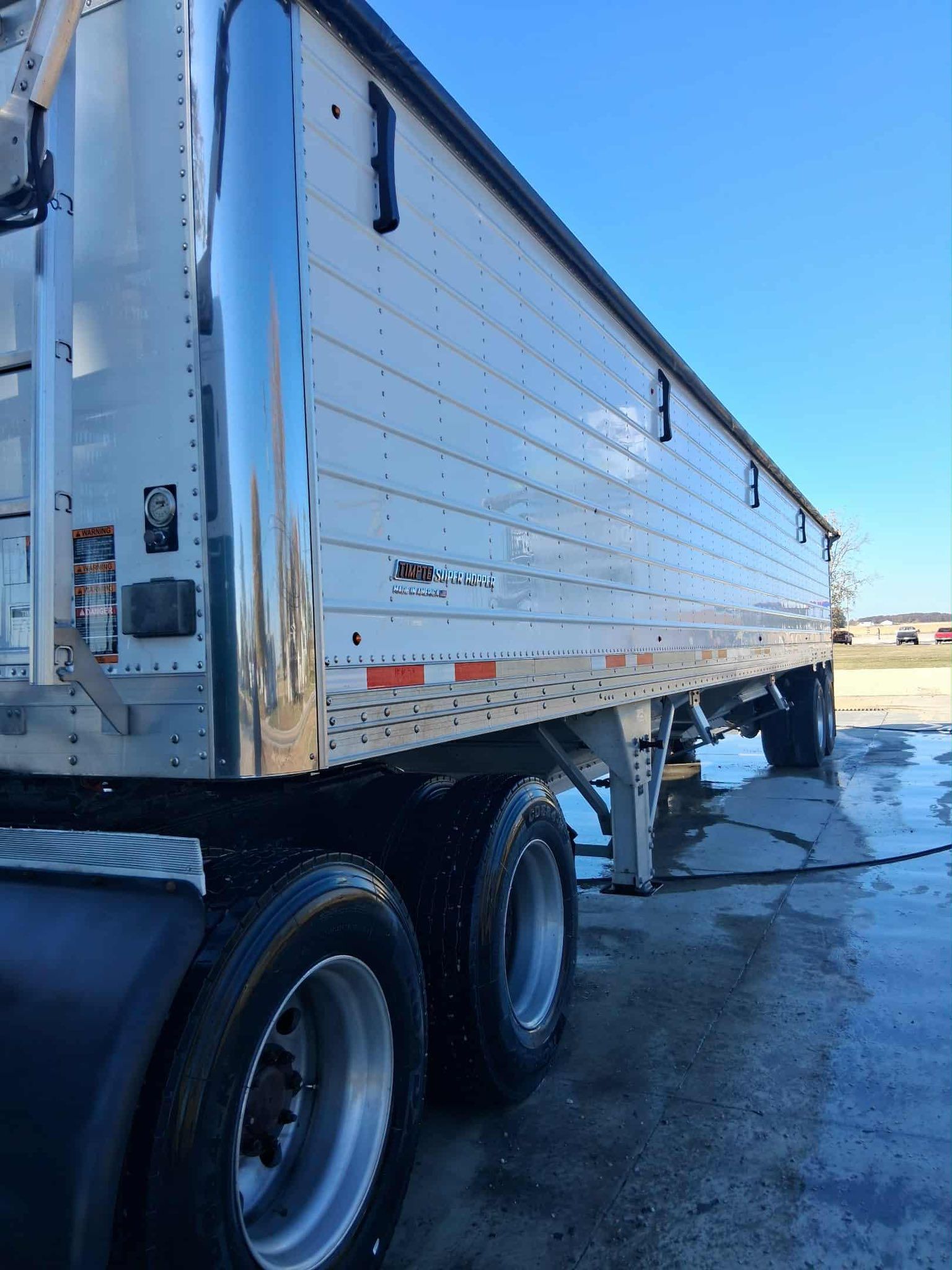 Silver grain trailer with black tires, parked under a blue sky.