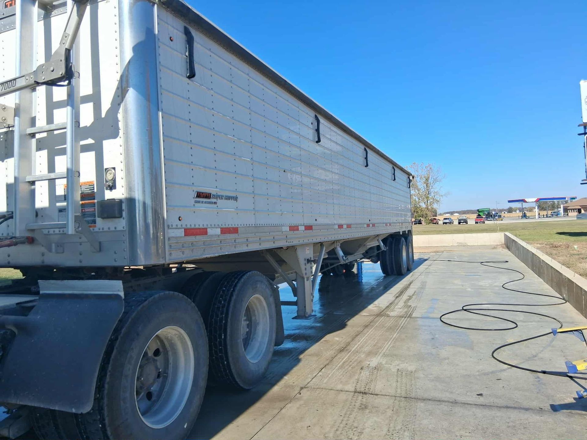 A large silver semi-trailer being washed outdoors on a sunny day.