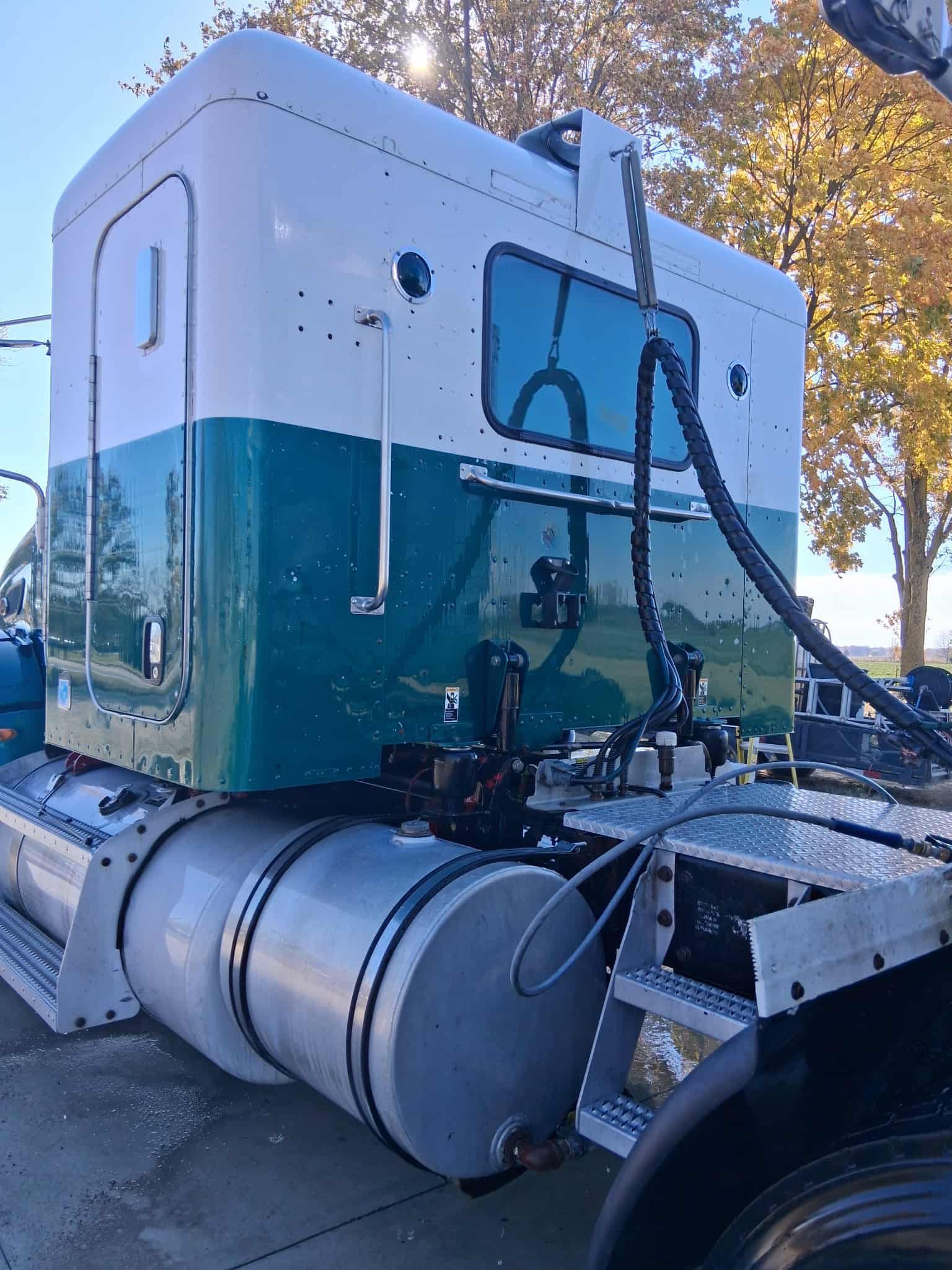 Two-tone green and white semi-truck cab with sleeper, parked outside on a sunny day.