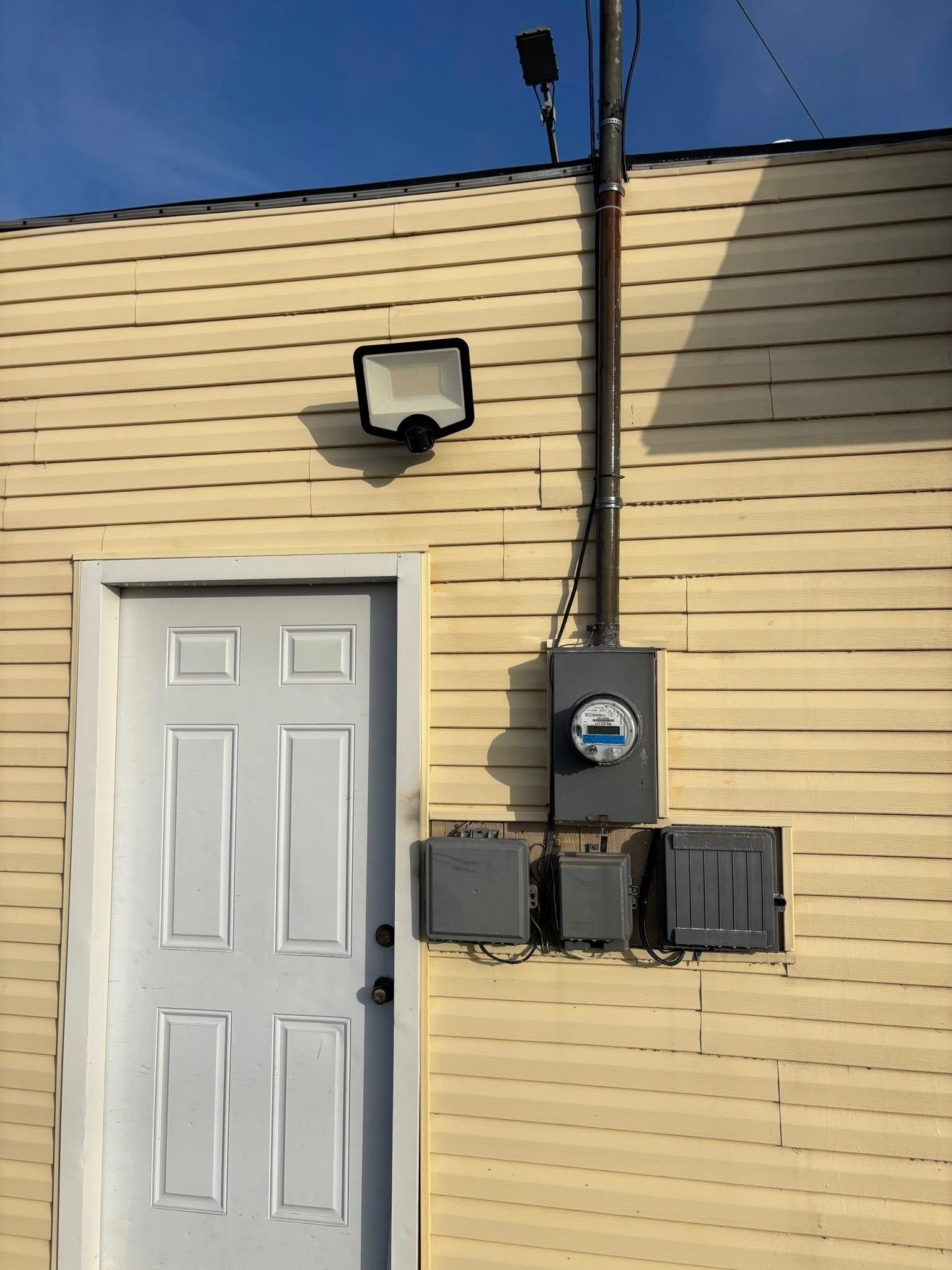 Exterior of building with white door, yellow siding, and electrical equipment attached.