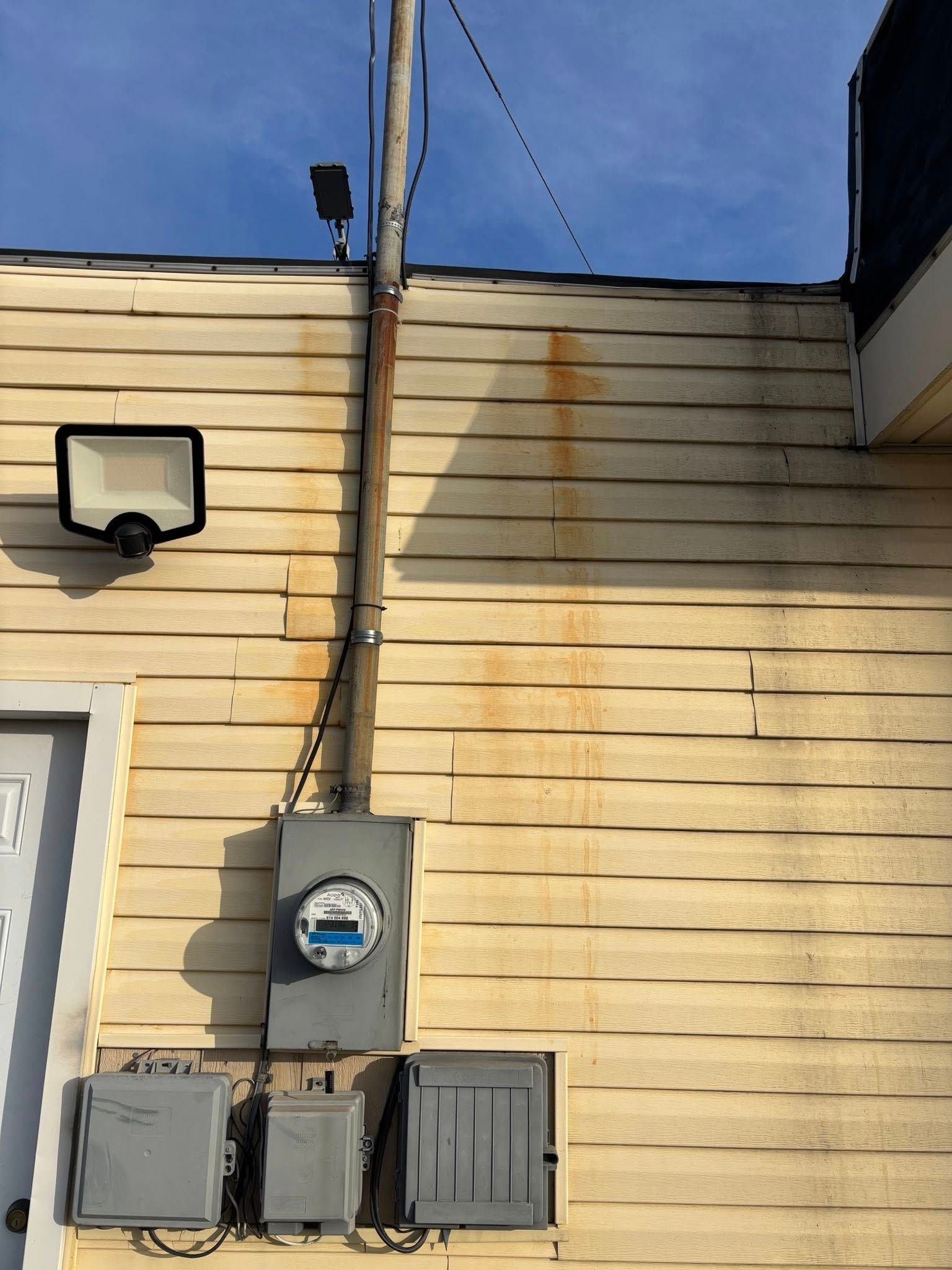 Exterior electrical panel and light fixture on a yellow-sided building. Brown streaks below.