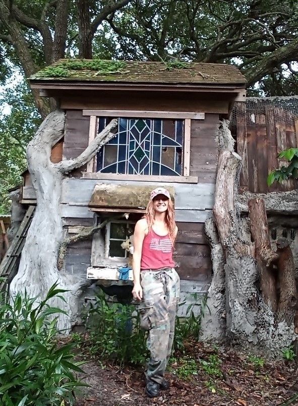 A woman in a red tank top is standing in front of a tree house