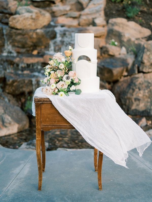 A wedding cake is sitting on a wooden table in front of a waterfall.