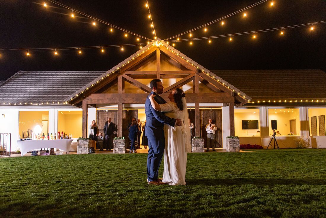 A bride and groom are dancing in front of a large house at night.