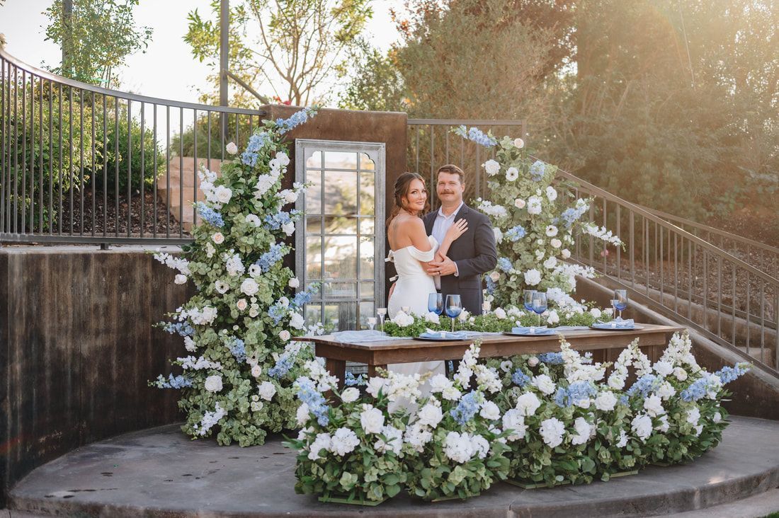 A bride and groom are standing in front of a table decorated with flowers.