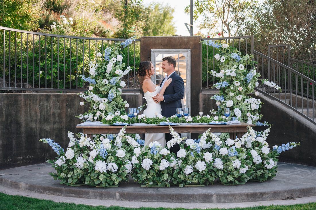 A bride and groom are standing in front of a table decorated with flowers.